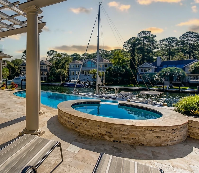 A shotcrete pool and raised spa beside a dock and moored sailboat